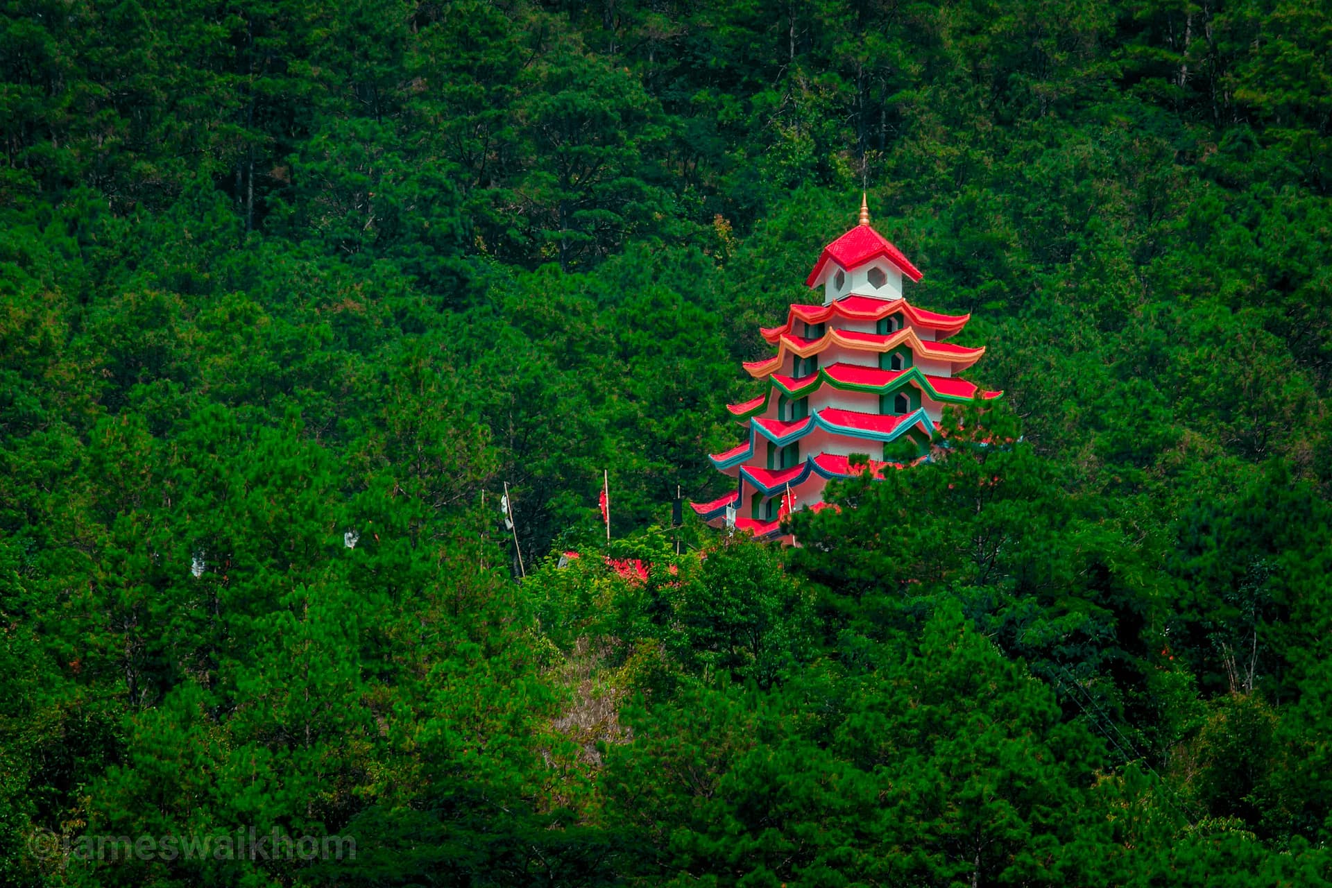 A red-roofed hill temple among dense green forest in Manipur